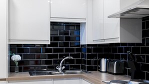 A modern kitchen with white cabinets, a black tiled backsplash, stainless steel appliances, and a wooden countertop. - Designer 1-bedroom in Kensington (London)