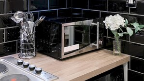 A kitchen with a black microwave, a stainless steel stove, and a white cabinet above. - Designer 1-bedroom in Kensington (London)