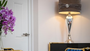 A dining area with a round white table, two blue velvet upholstered chairs with gold frames, a vase with purple flowers, and a wall-mounted lamp. - Designer 1-bedroom in Kensington (London)