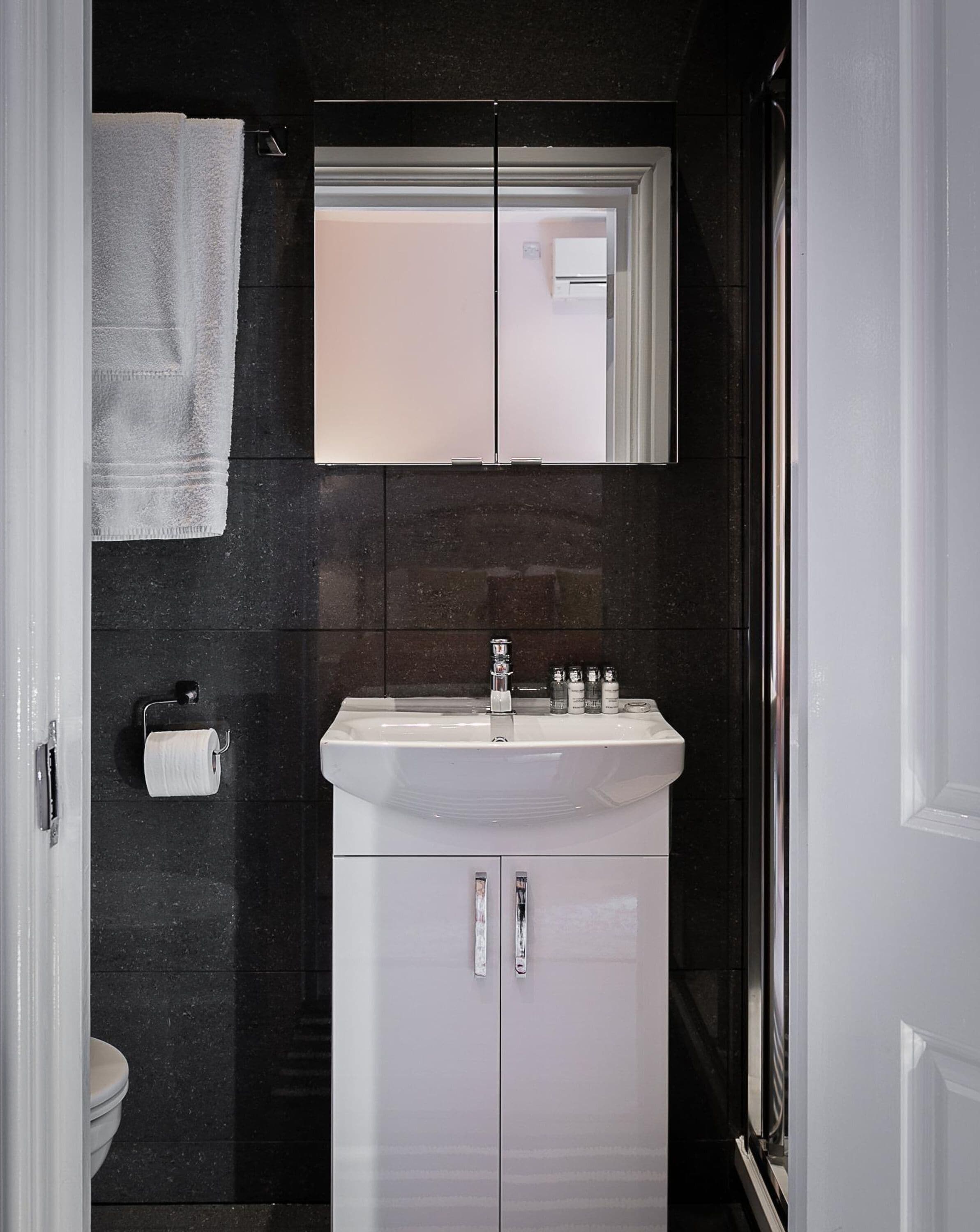 Et badeværelse med en hvid vask, to spejle, en håndklædestang og et toilet.