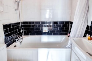 A bathroom with a white bathtub, black and white tiled walls, and a shower area. - Hardwood Home (London)