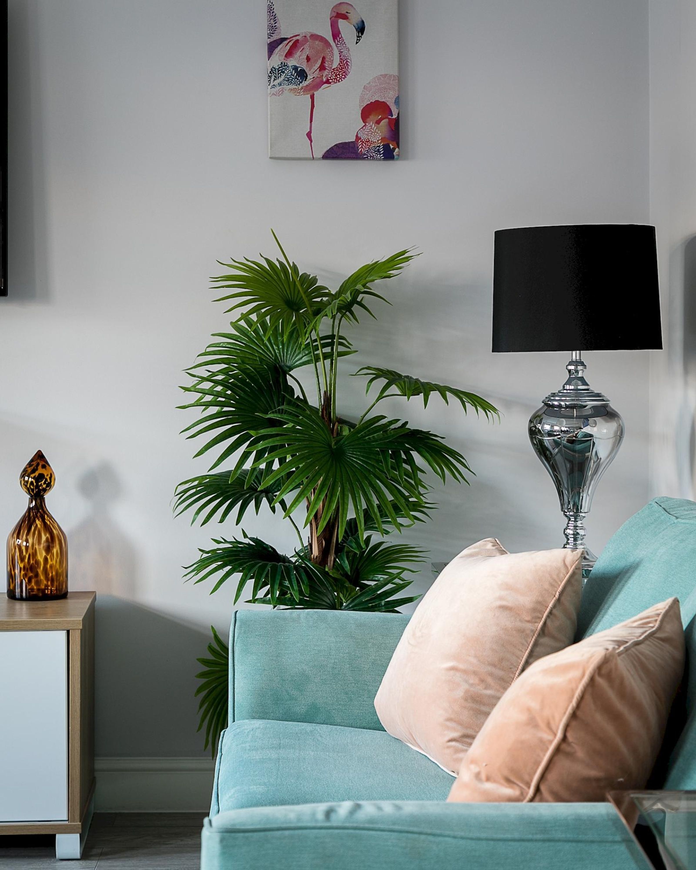 Een woonkamer met een blauwgroene bank, een potplant, een lamp en een lijst met kunstwerk aan de muur.