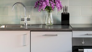 A modern kitchen with grey cabinets, a stainless steel sink, and a vase with purple flowers on the counter. - Stylish Modern 2-bedroom Apartment on Cromwell (London)