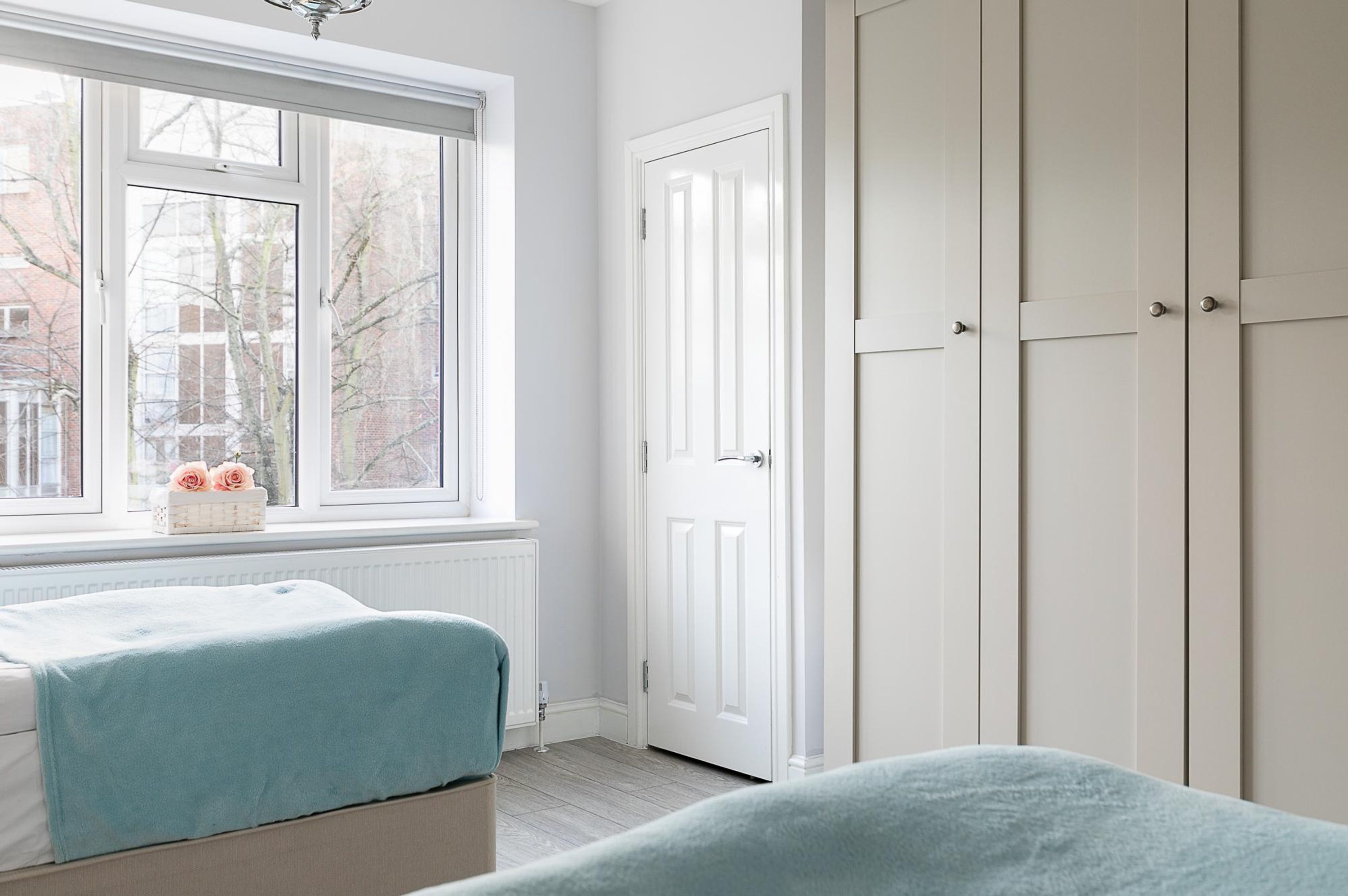 A bedroom with a large window, a bed, a wardrobe, and a radiator.