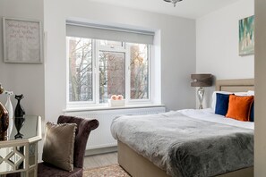 A bedroom with a bed, a window, a radiator, a lamp, and a painting on the wall. - Stylish Modern 2-bedroom Apartment on Cromwell (London)