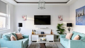 A modern living room with two teal sofas, a glass coffee table, a flat-screen TV, and decorative items. - Stylish Modern 2-bedroom Apartment on Cromwell (London)