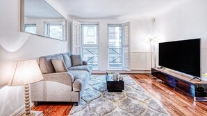 A modern living room with a sofa, a coffee table, a TV, and a large window with shutters. - At Home in Marylebone (London)