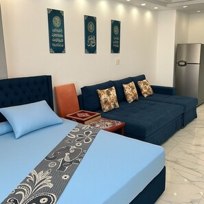 Ein modernes Schlafzimmer mit einem großen Bett, einem Schlafsofa und einem kleinen Tisch. Auf dem Schlafsofa liegen dekorative Kissen und ein Buch. Die Wand ist weiß und mit drei Dekorationselementen versehen.