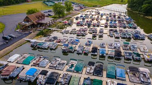 Una marina con numerose imbarcazioni ormeggiate, un'area parcheggio e un edificio con una rampa che conduce a un pontile.