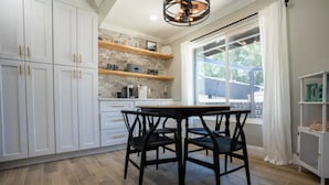 A modern kitchen with white cabinets, a black dining table, and a large window with white curtains.