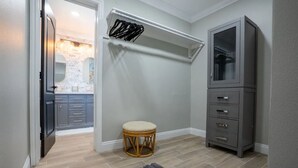A hallway with a wooden floor, a grey rug, a wicker stool, a grey cabinet, and a mirror on the wall.