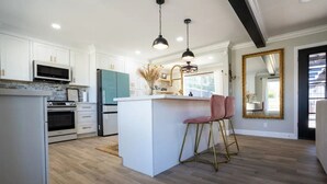 A modern kitchen with white cabinets, a central island, and a bar stool.