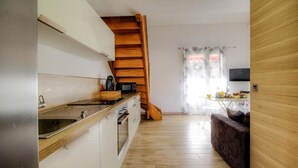 Cozinha compacta com piso de madeira, forno embutido e escada de madeira que dá acesso a uma área de refeições.