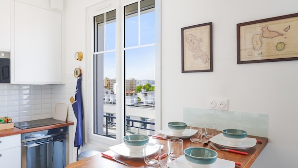Une cuisine moderne avec des meubles blancs, un plan de travail en bois et un coin repas aménagé pour quatre personnes.
