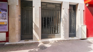Un bâtiment doté de trois grandes portes aux encadrements sombres et d’une petite fenêtre située au-dessus de la porte centrale.