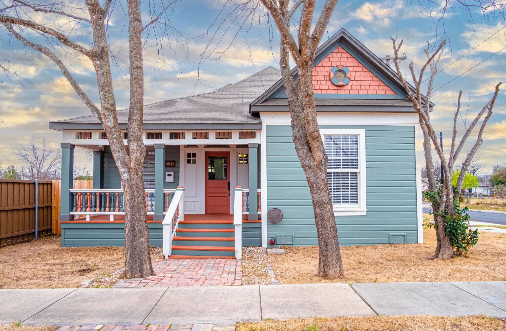 A single-story house with a front porch, a red door, and a small front yard.