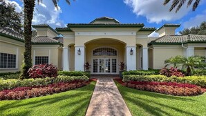 A well-maintained building with a central entrance, flanked by symmetrical landscaping and palm trees. - 14-208 Legacy Dunes, Lake View !, Close To Disney, Heated Swimming Pool (Kissimmee)