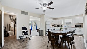 Une cuisine moderne avec des meubles blancs, un coin repas doté d’une table et de chaises en bois, et un ventilateur de plafond.