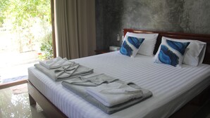 Een hotelkamer met een bed, handdoeken en uitzicht op groen.