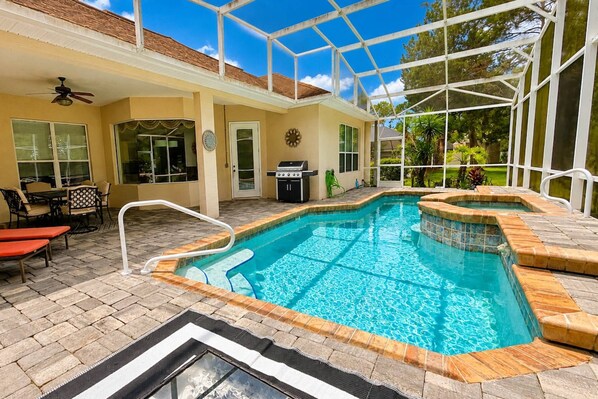 Una piscina con cerramiento de vidrio, mobiliario exterior y zona de barbacoa.