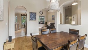 A dining area with a wooden table and chairs, a hanging light fixture, and a clock on the wall.