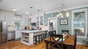 A modern kitchen with white cabinets, a central island, and a dining area with a wooden table and chairs.