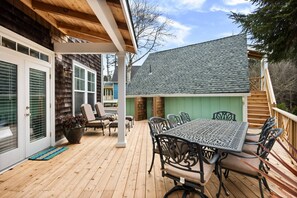 Eine Holzterrasse mit Tisch und Stühlen, ein überdachter Bereich mit einer Pergola und ein Haus mit Schindeldach.