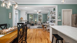 A kitchen with wooden flooring, a white countertop, and a dining area with a bench and chairs.