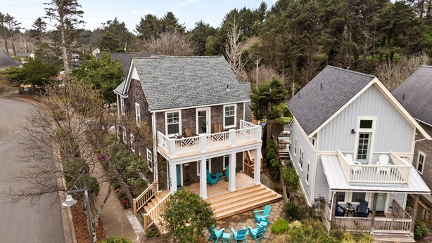 A two-story house with a porch and a small deck, surrounded by trees.