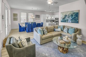 A modern living room with a beige sectional sofa, blue chairs, a glass coffee table, and a large abstract painting.