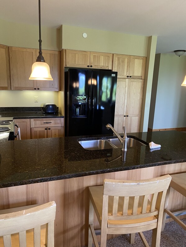 A kitchen with wooden cabinets, a black refrigerator, a sink, and a granite countertop.