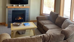 Ein Wohnzimmer mit Kamin, Fernseher, Deckenventilator und einem großen Fenster.