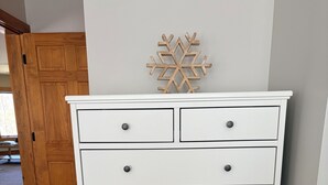 Une commode blanche avec des tiroirs et des boutons, une porte en bois en arrière-plan et un décor en forme de flocon de neige sur le mur.