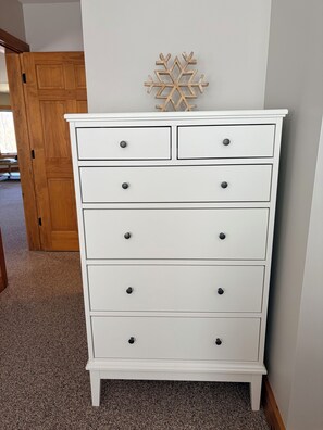 A white dresser with drawers and knobs, a wooden door in the background, and a snowflake decoration on the wall.