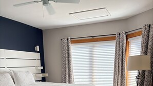 Ein Schlafzimmer mit Bett, Deckenventilator, einem Fenster mit Vorhängen und einer Stehlampe.