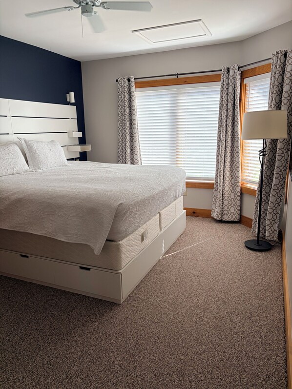 A bedroom with a bed, a ceiling fan, a window with curtains, and a floor lamp.