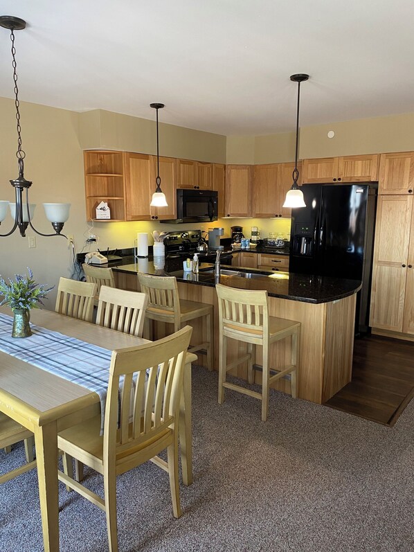 Una cocina con armarios de madera, un refrigerador negro, una estufa y un comedor con mesa y sillas.