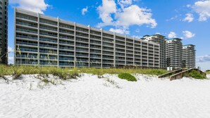 Ein modernes Hotel mit mehreren Etagen, ein Sandstrand im Vordergrund und ein klarer, blauer Himmel.