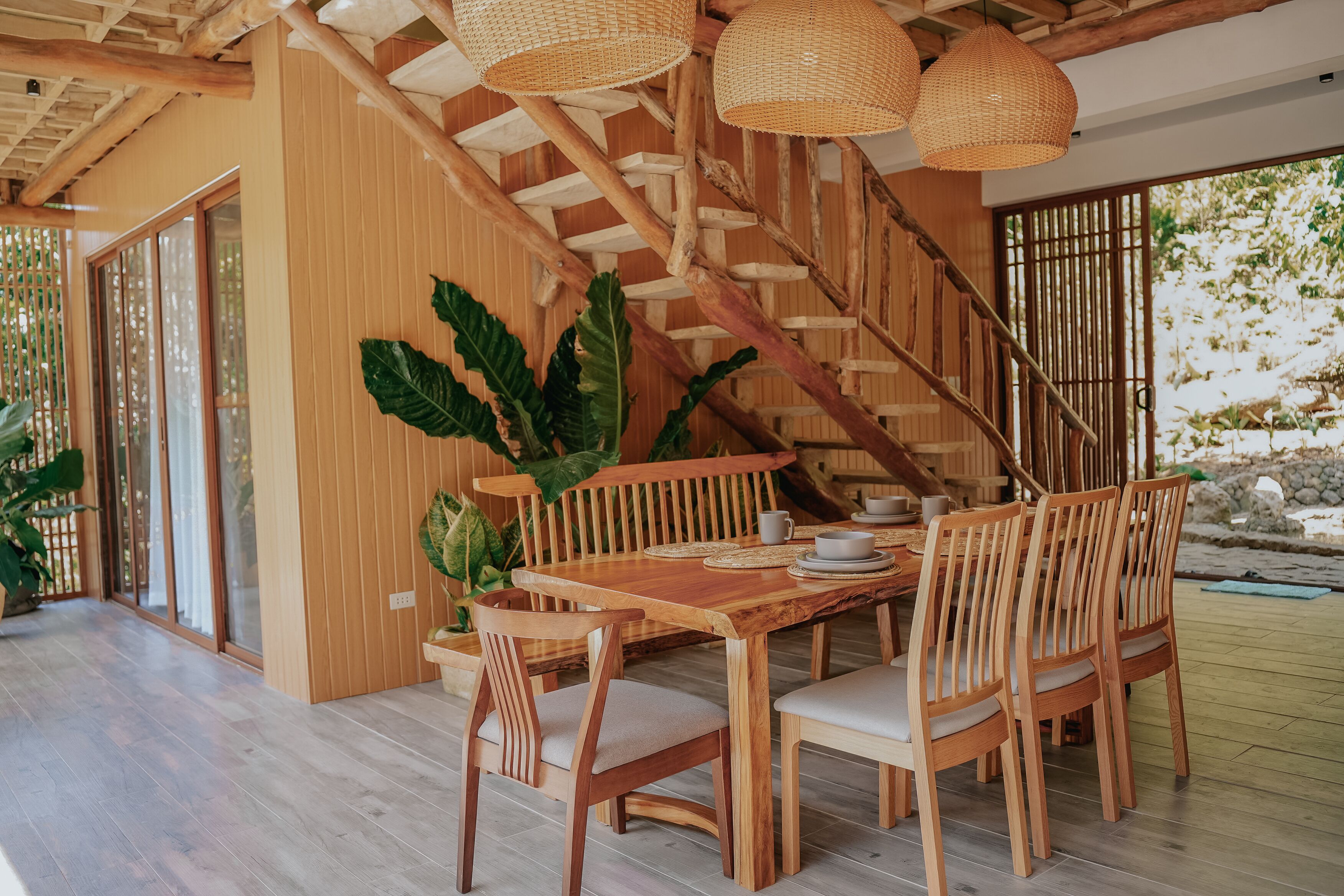 A wooden dining table with chairs, a staircase, and woven light fixtures.