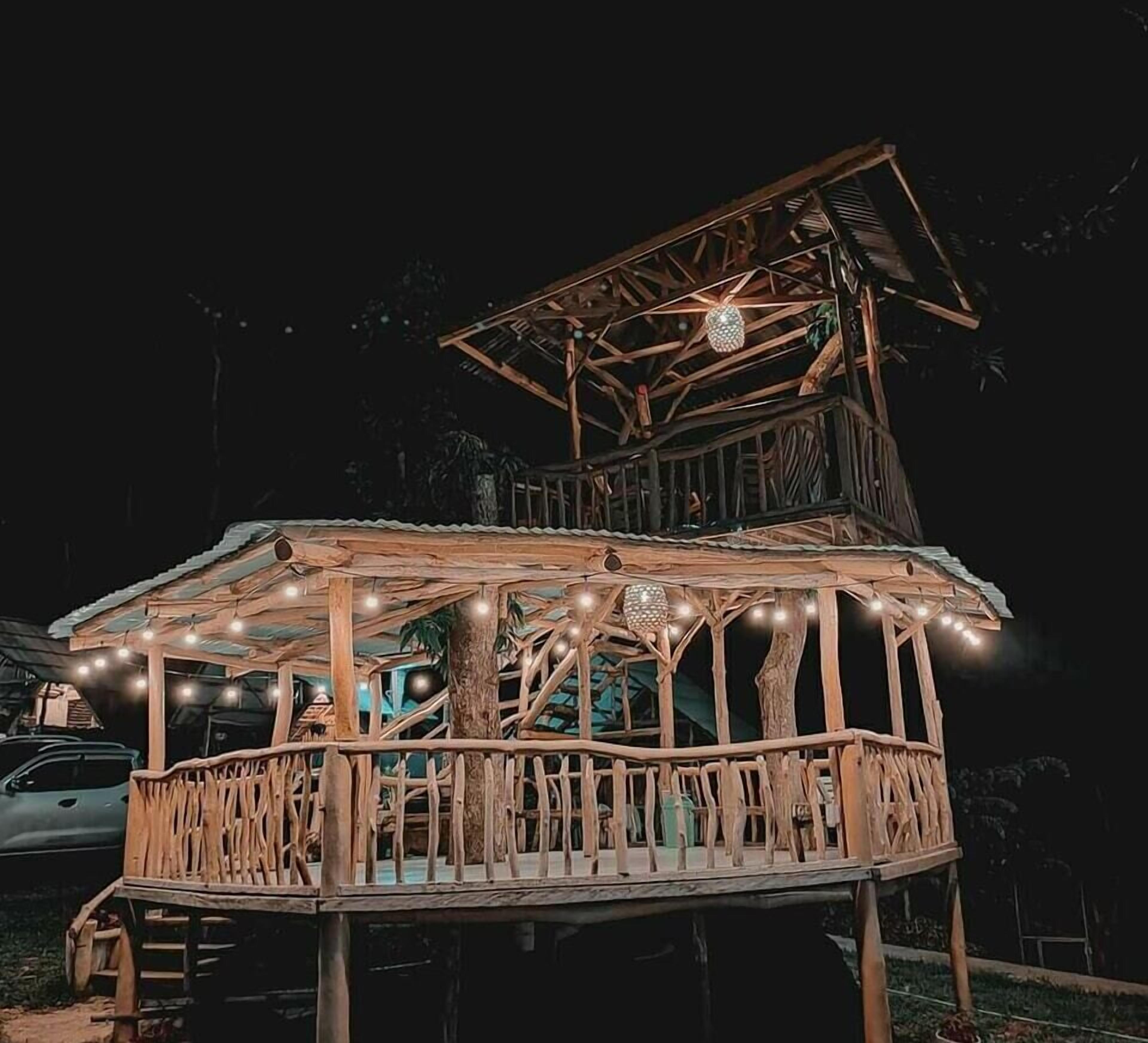 A wooden gazebo with a tiered roof, string lights, and a car parked nearby.