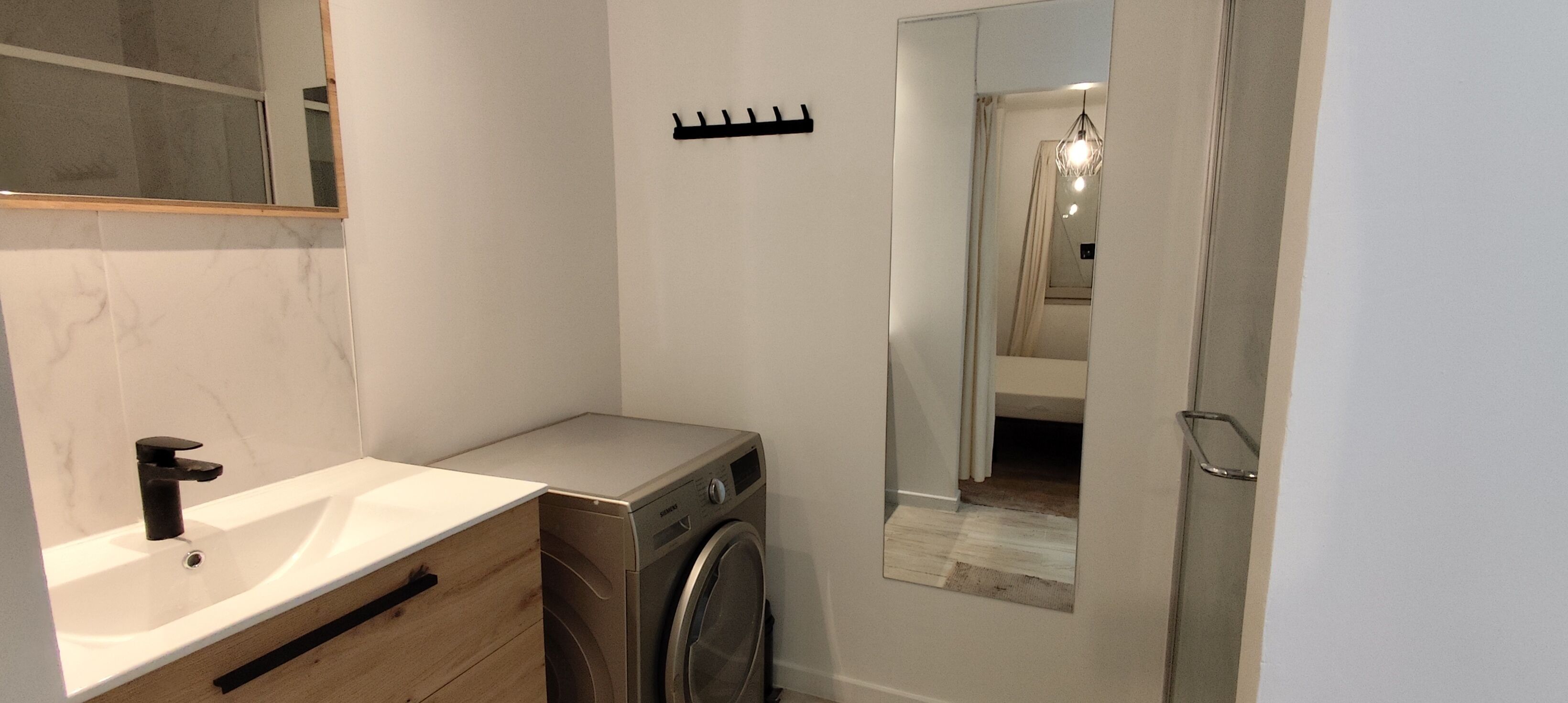 Un baño pequeño con un lavamanos, lavadora y espejo.
