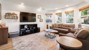 A modern living room with a flat-screen TV, a sofa, a coffee table, and a bookshelf. - Pacifica Storybook Beach House, 2 blocks from beach, pier and golf, 10 min to SF (Pacifica)