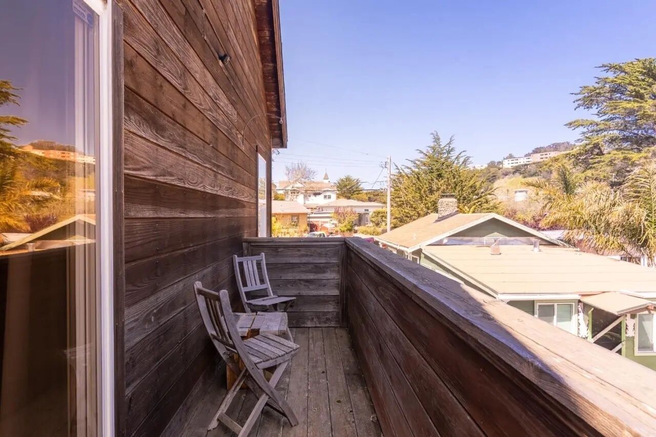 Un balcon en bois avec deux chaises et une vue sur les maisons et les arbres environnants.