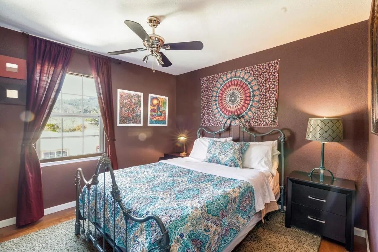 A bedroom with a bed, a ceiling fan, a nightstand, and a window with curtains.