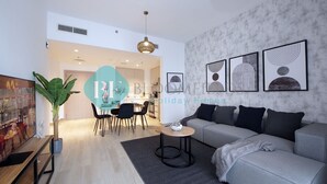 A modern living room with a grey sofa, a round coffee table, and a dining area with chairs and a table. - Cozy Canal View Apartment (Abu Dhabi)
