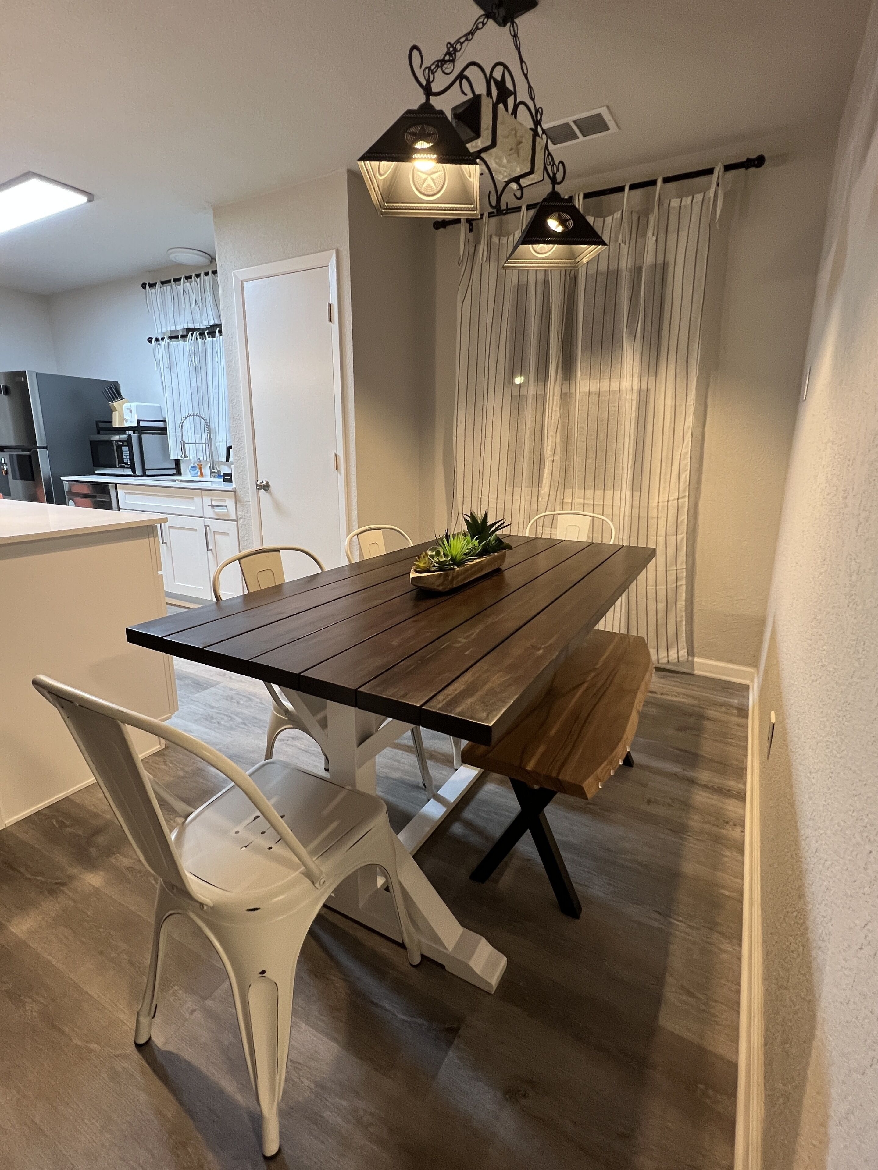 A dining area with a wooden table, white chairs, and a plant centerpiece.