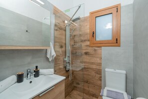 Um banheiro moderno com box de vidro, armário de madeira, pia branca e vaso sanitário.