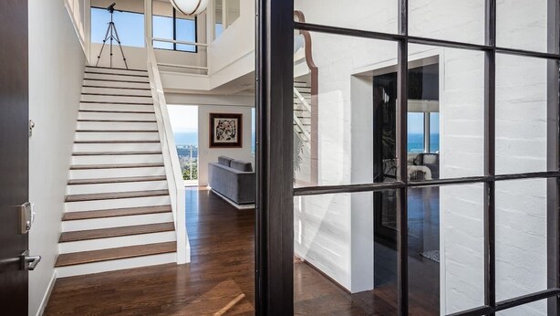 A modern interior with a wooden staircase leading to a loft area, a large window, and a view of the sky.
