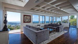 A spacious living room with a large gray sectional sofa, a glass coffee table, and a view of the ocean.
