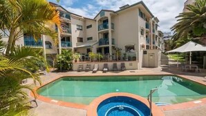 A multi-story hotel with a swimming pool, outdoor seating, and palm trees. - Aruba Beach - Private Apartments (Broadbeach)